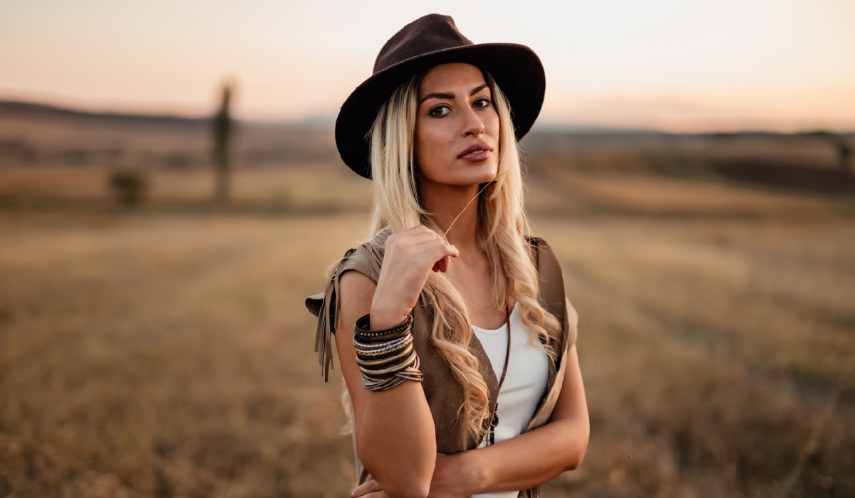 Portrait of a bohemian styled young woman with blond hair wearing a hat in nature field on a sunny summer day
