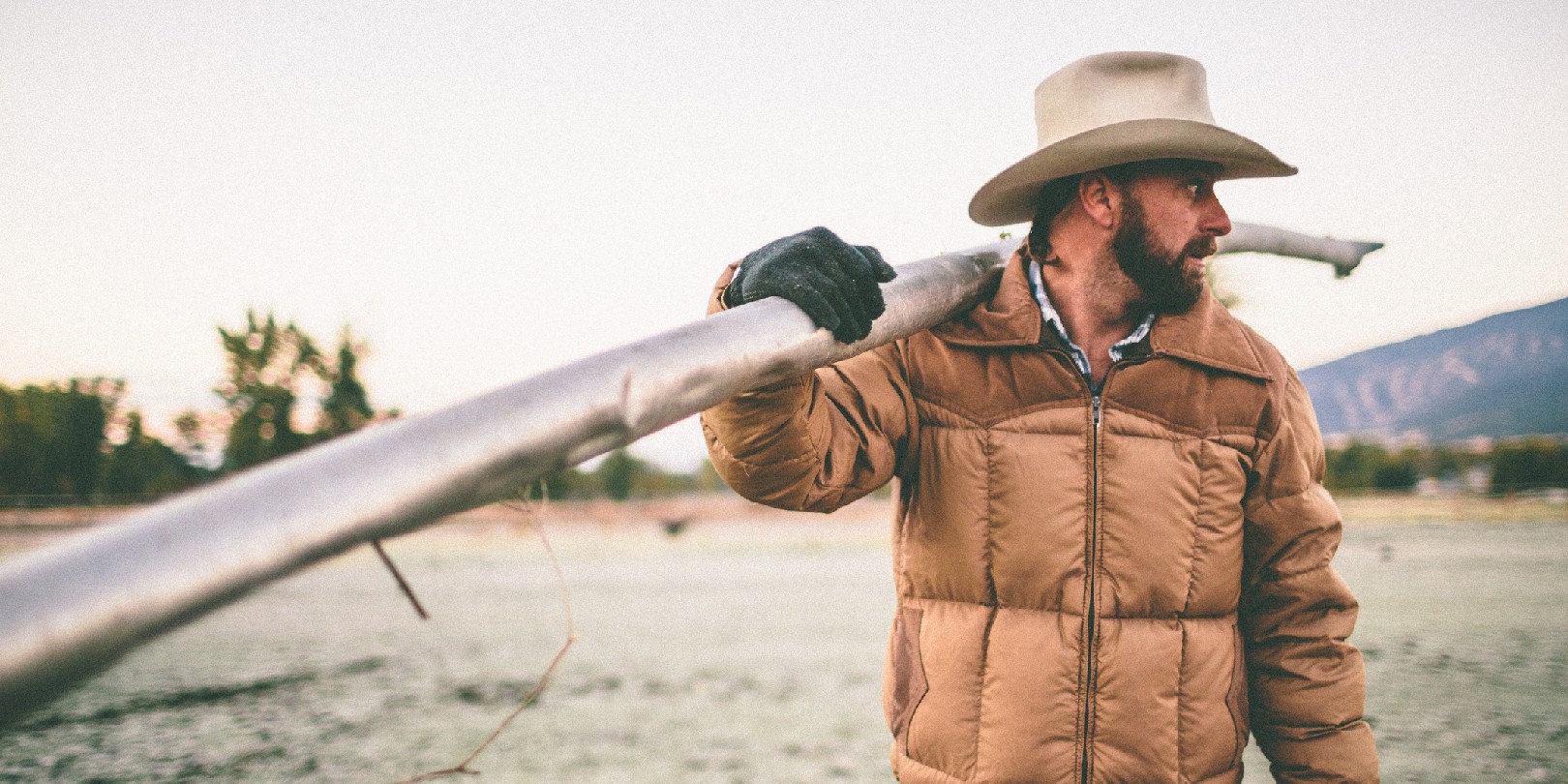 Man standing in field carries irrigation pipe over shoulder